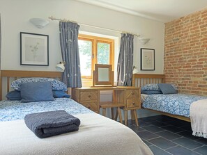Ein Schlafzimmer mit zwei Betten, einem Holztisch, einem Stuhl, einem Spiegel und einem Fenster mit Vorhängen.