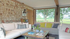 A living room with a stone wall, a sofa, a coffee table with magazines, and a bookshelf. - 6 bedroom accommodation in Oxborough (Oxborough)