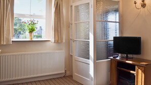 A room with a radiator, a window with curtains, a television on a wooden stand, and a wall-mounted light fixture. - 1 bedroom accommodation in Peak Forest, near Buxton (Peak Forest, near Buxton)