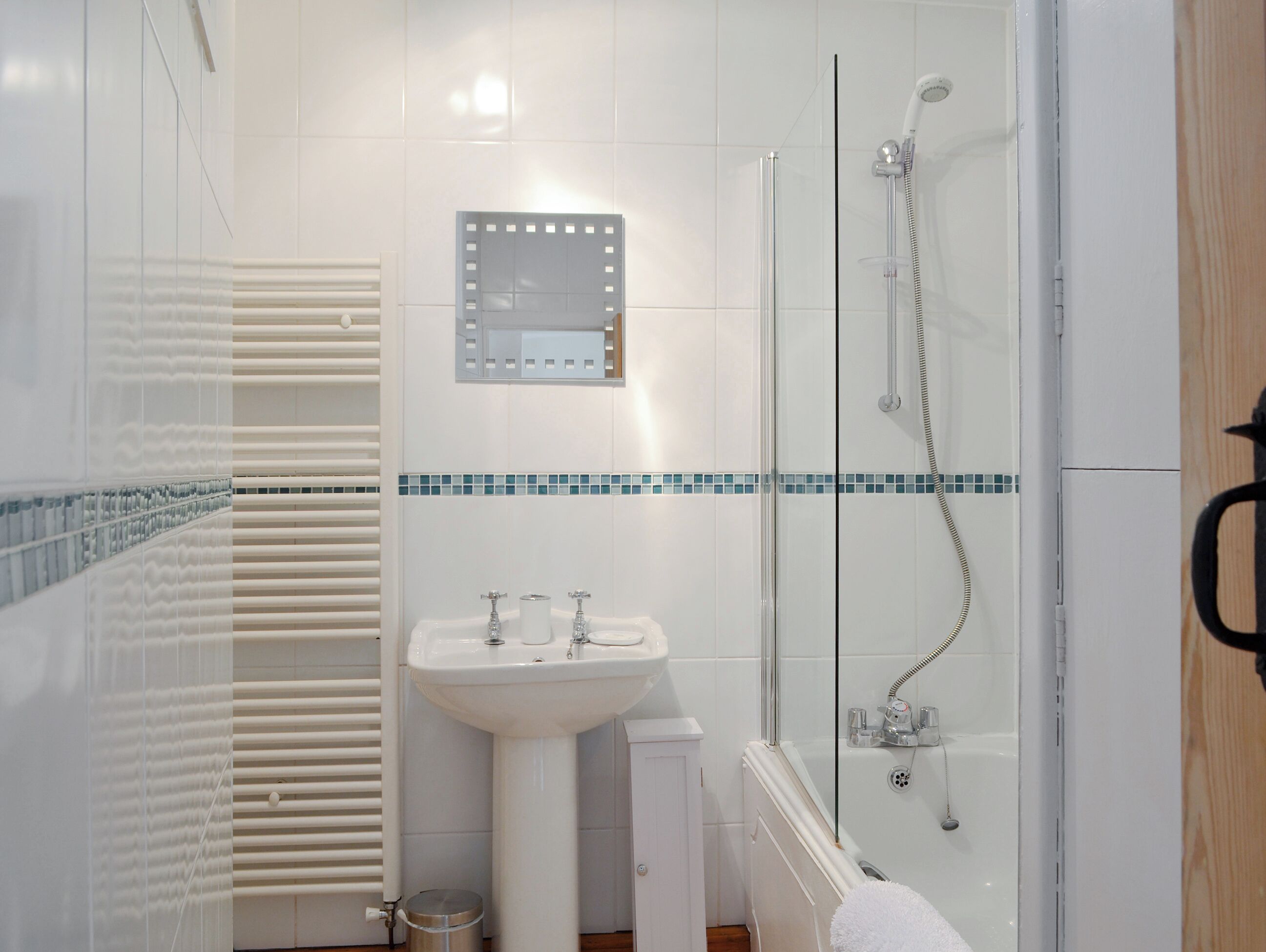A bathroom with a glass-enclosed shower, a white sink, and a mirror with lights.