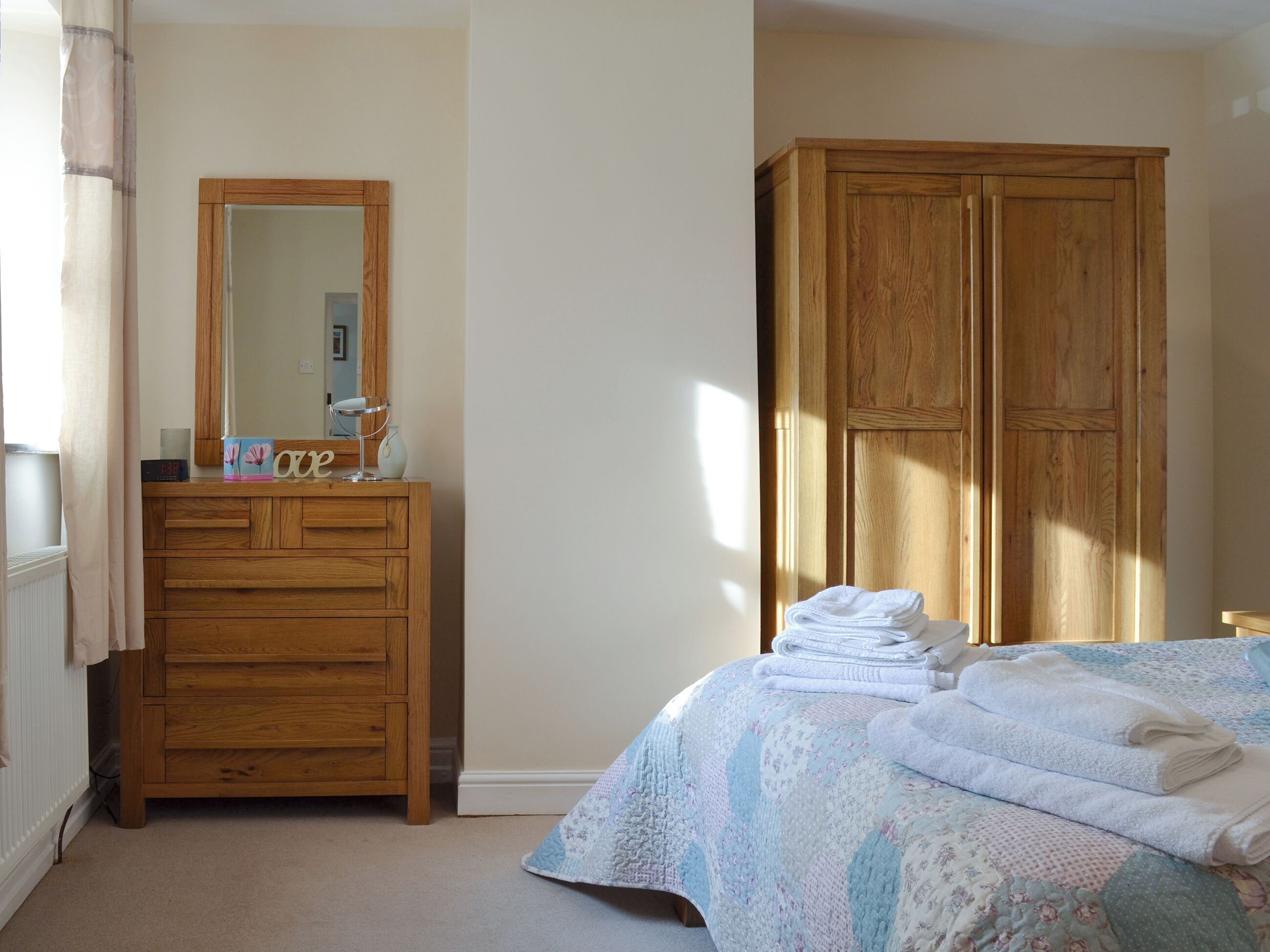 A bedroom with a wooden dresser, a bed with a quilt, a mirror, and a wardrobe.