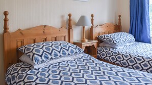 Een tweepersoonsbed met een geborduurde sprei, een houten hoofdbord, een nachtkastje met een lamp en een aan de muur hangend schilderij.
