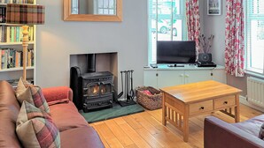 Ein gemütliches Wohnzimmer mit Kamin, einer Couch, einem Couchtisch aus Holz und einem Bücherregal.