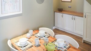 Ein Essbereich mit einem Holztisch, gedeckt für vier Personen, weißen Stühlen, einer grünen Teekanne und einer gerahmten Karte an der Wand.