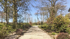 Un chemin de gravier bordé d’arbres et d’arbustes, qui mène à un bâtiment.