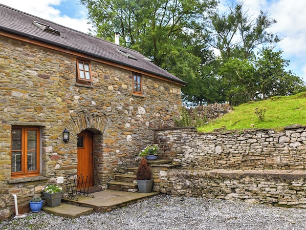 A stone house with a wooden door, a small porch, and a stone wall.