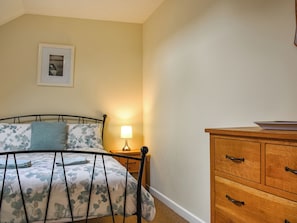 Ein Schlafzimmer mit einem Bett, einem Nachttisch mit Lampe, einer Holzkommode und einem gerahmten Bild an der Wand.