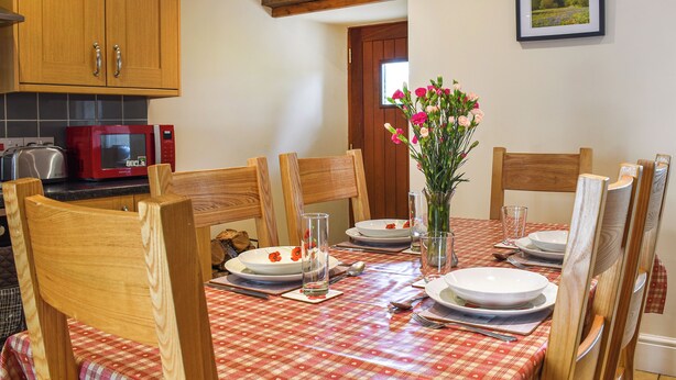 A dining area with a red and white checkered tablecloth, wooden chairs, a vase with flowers, and a red microwave.