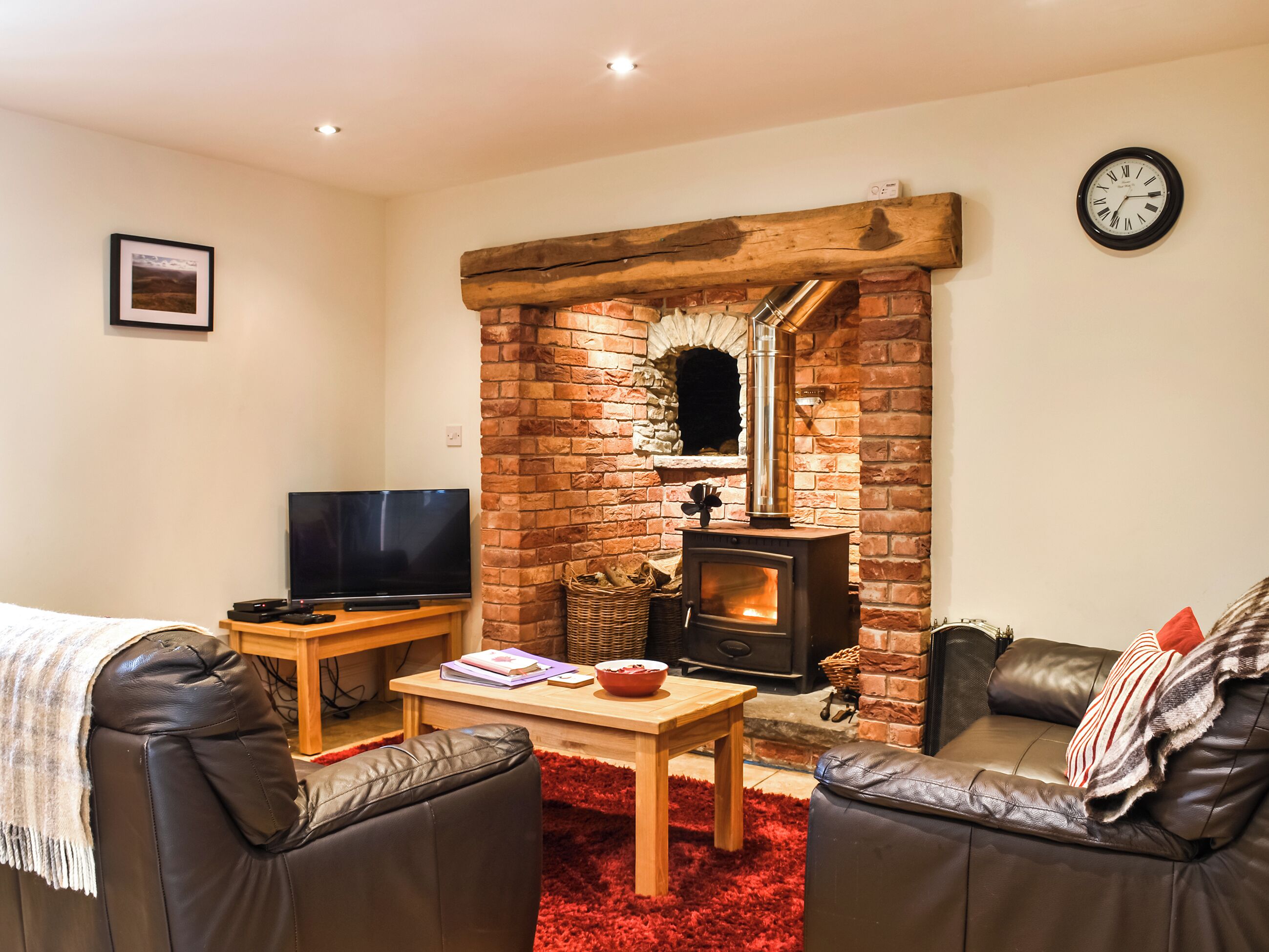 A cozy living room with a brick fireplace, leather sofas, a television, and a red rug.