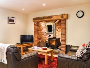 Ein gemütliches Wohnzimmer mit Kamin aus Backstein, Ledersofas, einem Fernseher und einem roten Teppich.