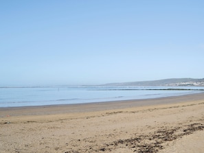 Ein weiter Sandstrand mit sanften Wellen, blauem Himmel und Hügeln im Hintergrund.