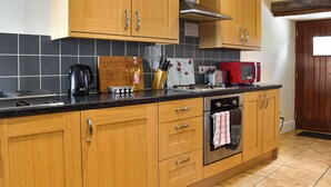 Een keuken met houten kastjes, een zwart aanrecht, een broodrooster, een waterkoker en een rode magnetron.