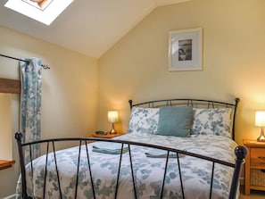 A bedroom with a bed, a nightstand, a lamp, a framed picture on the wall, and a window with a curtain.