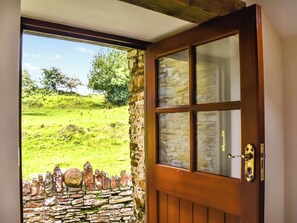 A wooden door with a glass panel, leading to a stone wall and a grassy landscape with trees.
