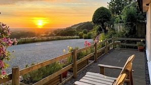 Eine Holzterrasse mit Blick auf einen Fluss und einen Sonnenuntergang.