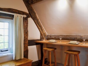 A rustic dining area with a wooden table, two stools, and a window with a curtain.