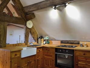 A kitchen with wooden cabinets, a white sink, a stove, and a clock on the wall.
