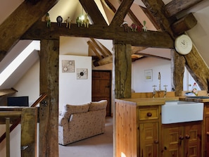 A rustic kitchen with wooden beams, a sofa, and a clock on the wall.