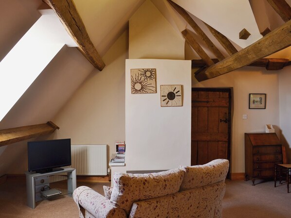 A cozy loft bedroom with a sloped ceiling, exposed wooden beams, a bed, a dresser, and a television on a stand.
