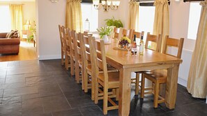 Uma sala de jantar com mesa e cadeiras de madeira, um lustre e vista para a sala de estar.