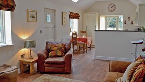 A cozy living room with a leather armchair, a wooden coffee table, and a patterned rug. There is a dining area with a table and chairs, and a kitchen area with a bar stool. - 1 bedroom accommodation in Moor Monkton, near York (Moor Monkton, near York)