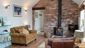 A cozy living room with a brick fireplace, leather sofas, and a glass coffee table. - 1 bedroom accommodation in Moor Monkton, near York (Moor Monkton, near York)