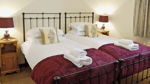 Una cama doble con sábanas blancas, dos mesitas de noche con lámparas, una mesita auxiliar de madera, una manta roja y un cuadro en la pared.