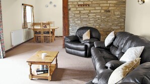 Una sala de estar acogedora con pared de piedra, sofá de cuero, mesa de centro de madera y comedor con mesa y sillas.
