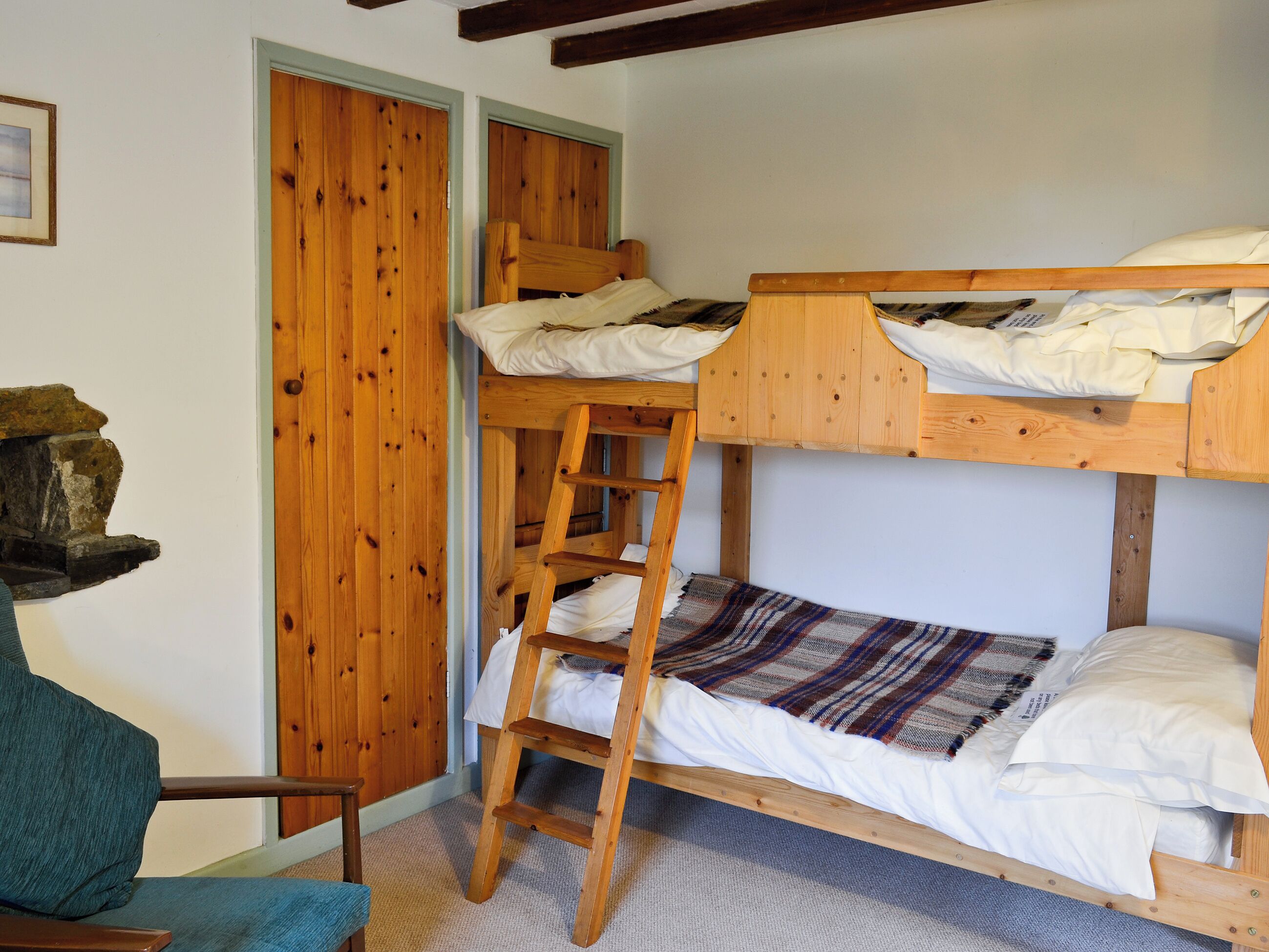 A bunk bed with a ladder, a chair, and a wooden wall with a stone feature.