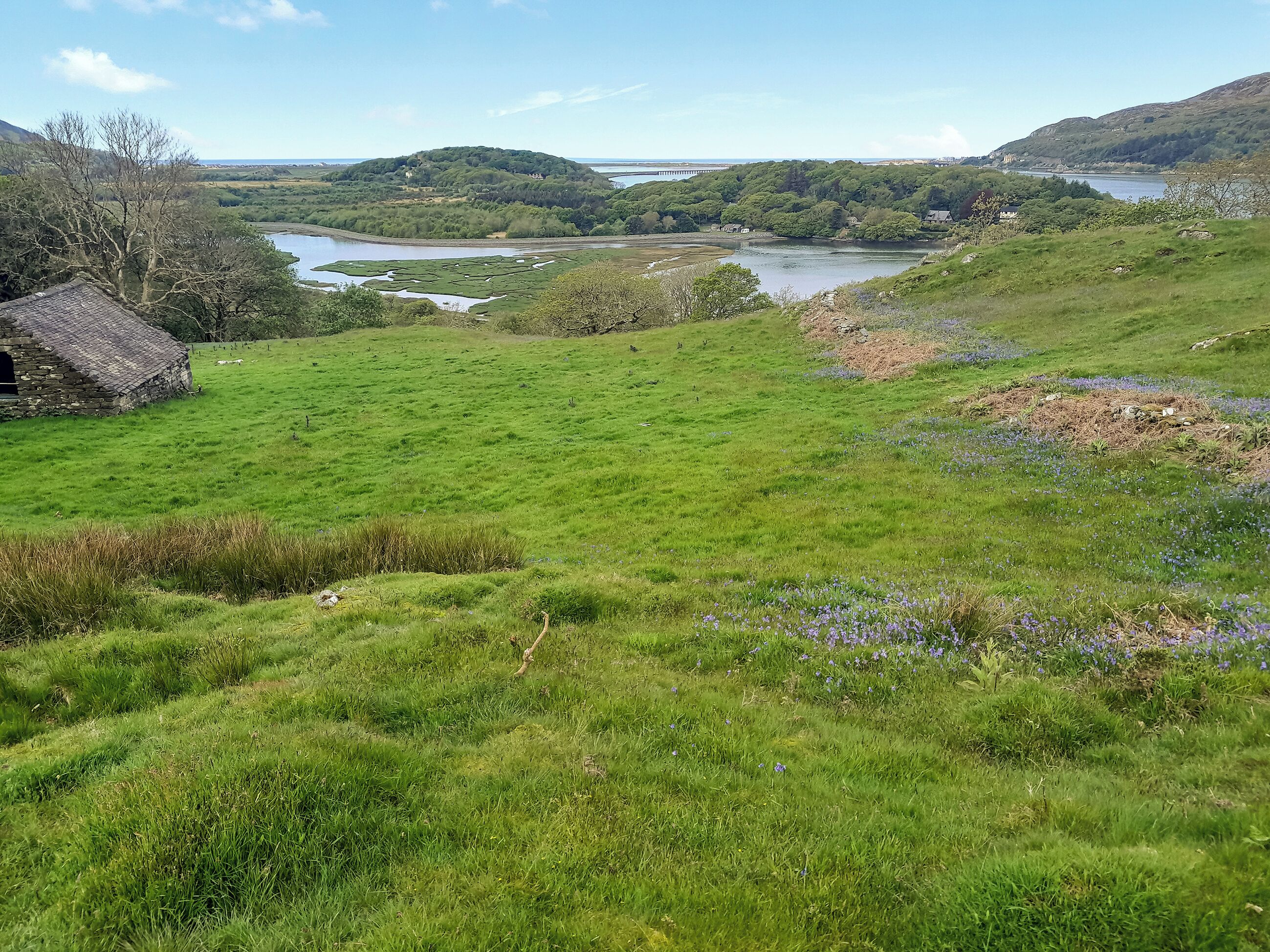 A rural landscape with a stone house, green fields, and a lake.