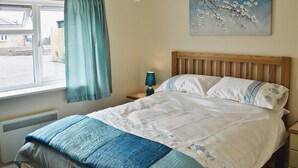 Una cama bien hecha con colcha azul y blanca, un cabecero de madera y una ventana con cortinas.