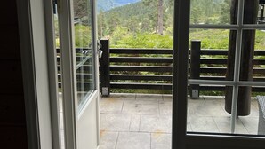 Uitzicht door een deur op een balkon met een stenen vloer, een houten hek en een berglandschap.