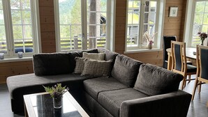 Een moderne woonkamer met een modulaire bank, een glazen salontafel en grote ramen met uitzicht op het landschap.