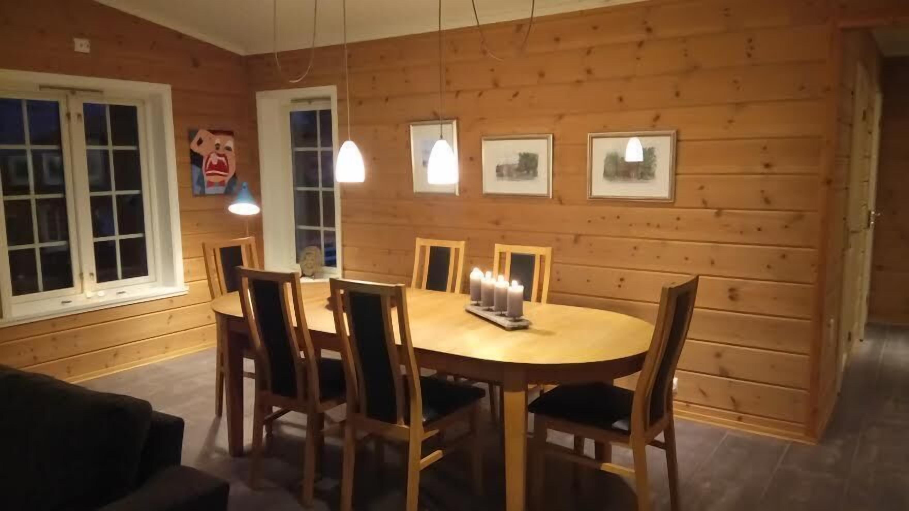 A wooden-paneled dining room with a round table, chairs, and hanging pendant lights.