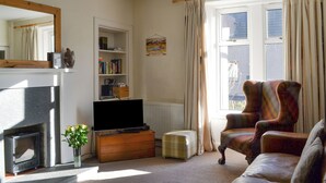 A living room with a fireplace, television, bookshelf, and a plaid armchair. - 2 bedroom accommodation in Kingussie (Kingussie)