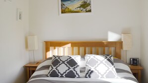 A neatly made bed with striped bedding and patterned pillows, a wooden headboard, and a framed coastal landscape painting above it. - 2 bedroom accommodation in Kingussie (Kingussie)