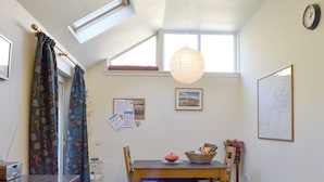 A compact kitchen with a dining area, a clock, and a window with curtains. - 2 bedroom accommodation in Kingussie (Kingussie)