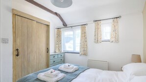 A bedroom with a wooden wardrobe, a bed with white bedding, a blue blanket, and floral curtains. - 2 bedroom accommodation in St Breward, Bodmin Moor (St Breward, Bodmin Moor)