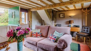 A cozy room with a wooden ceiling, a sofa with pillows, a vase of flowers, and a window with green shutters. - 1 bedroom accommodation in Brockdish, near Harleston (Brockdish, near Harleston)
