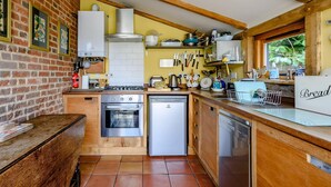 A kitchen with a brick wall, wooden beams, a gas stove, an oven, a dishwasher, and a window with a view of greenery. - 1 bedroom accommodation in Brockdish, near Harleston (Brockdish, near Harleston)