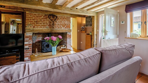 A cozy living room with exposed wooden beams, a brick fireplace, and a modern sofa. - 1 bedroom accommodation in Brockdish, near Harleston (Brockdish, near Harleston)