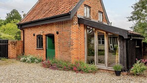 A small brick house with a sloped roof, a green door, and a window with a wooden frame. - 1 bedroom accommodation in Brockdish, near Harleston (Brockdish, near Harleston)