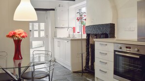 A compact kitchen with white cabinets, a built-in oven, and a dining area with a glass table and chairs. - 1 bedroom accommodation in Keswick (Keswick)