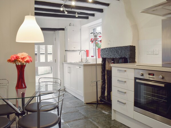 A compact kitchen with white cabinets, a built-in oven, and a dining area with a glass table and chairs. - 1 bedroom accommodation in Keswick (Keswick)