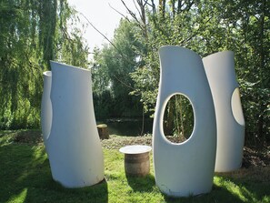 Tres esculturas grandes y blancas, de diseño abstracto, en un área exterior con césped, árboles y una masa de agua al fondo.