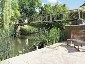 A wooden bridge over a calm river, surrounded by lush greenery and a bench on the right. - 1 bedroom accommodation in Barford, near Stratford-upon-Avon (Barford, near Stratford-upon-Avon)
