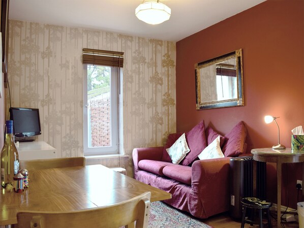 Une pièce avec une table à manger en bois, un canapé violet, un miroir au mur et un radiateur.