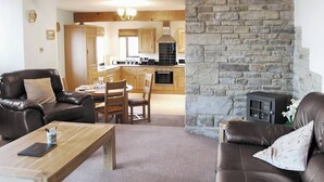 A cozy living room with a fireplace, leather sofas, a wooden coffee table, and a dining area with a kitchen in the background. - Ground Floor: 
Open plan living space. (Silsden near Skipton)