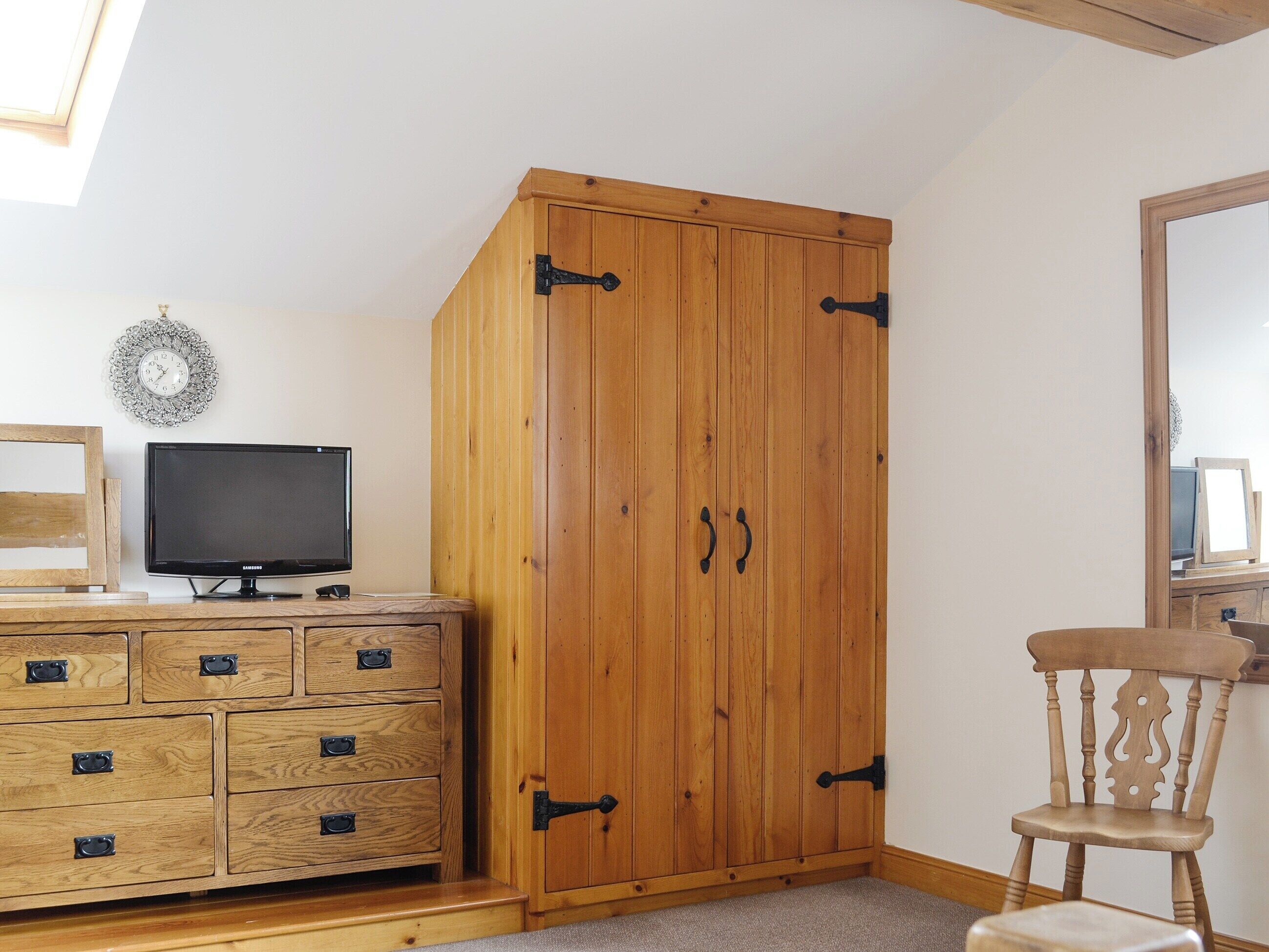 Una habitación con un armario de madera, un televisor en una cómoda y una silla.