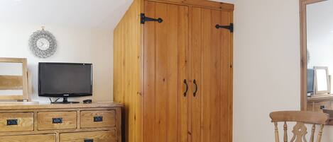 Una habitación con un armario de madera, un televisor en una cómoda y una silla.